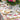 Outdoor table setting with floral tablecloth, plates, glasses, and a large bouquet of flowers.