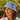 A woman wearing a light blue and white patterned bucket hat and a white collared shirt, photographed outdoors in a sunny garden setting.