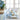 Dining table set with blue and white tablecloth, napkins, and decor in a bright room.